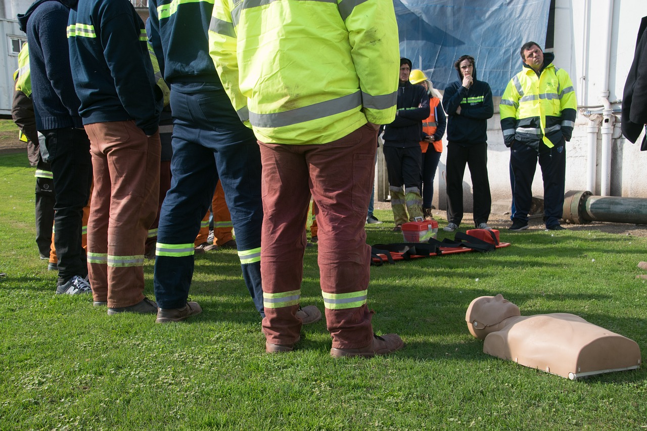 Workers in safety clothing listening to someone out of frame, with a CPR manikin on the ground.