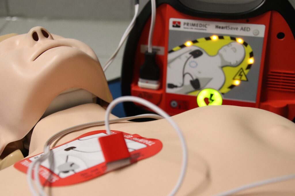 CPR manikin with training AED pad attached, training AED in background.